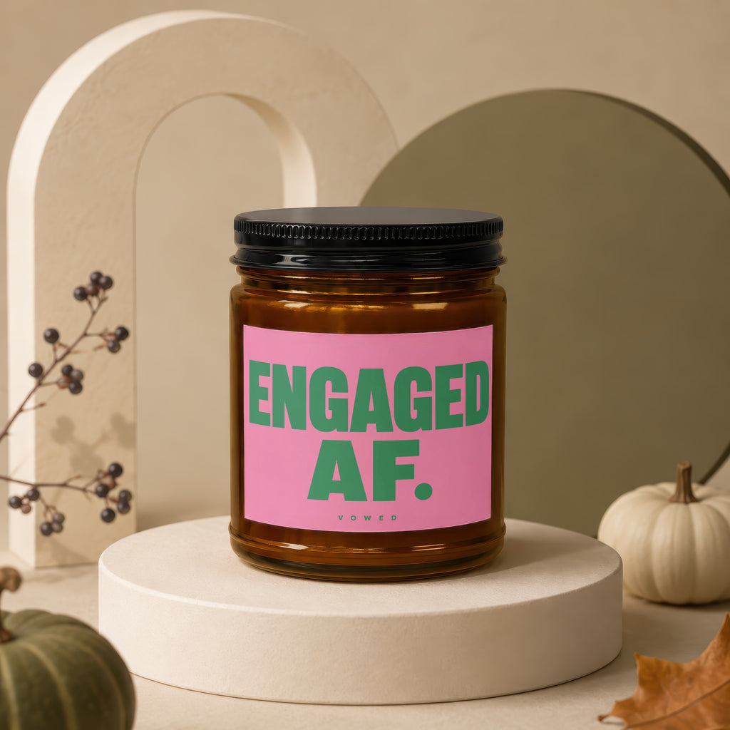 Amber jar candle with pink label reading "ENGAGED AF. VOWED" on a display stand.