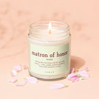 Glass jar candle with lit wick, "matron of honor" text and definition.