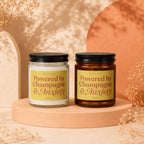 Two candles with labels reading "Powered by Champagne & Anxiety" on a display pedestal.