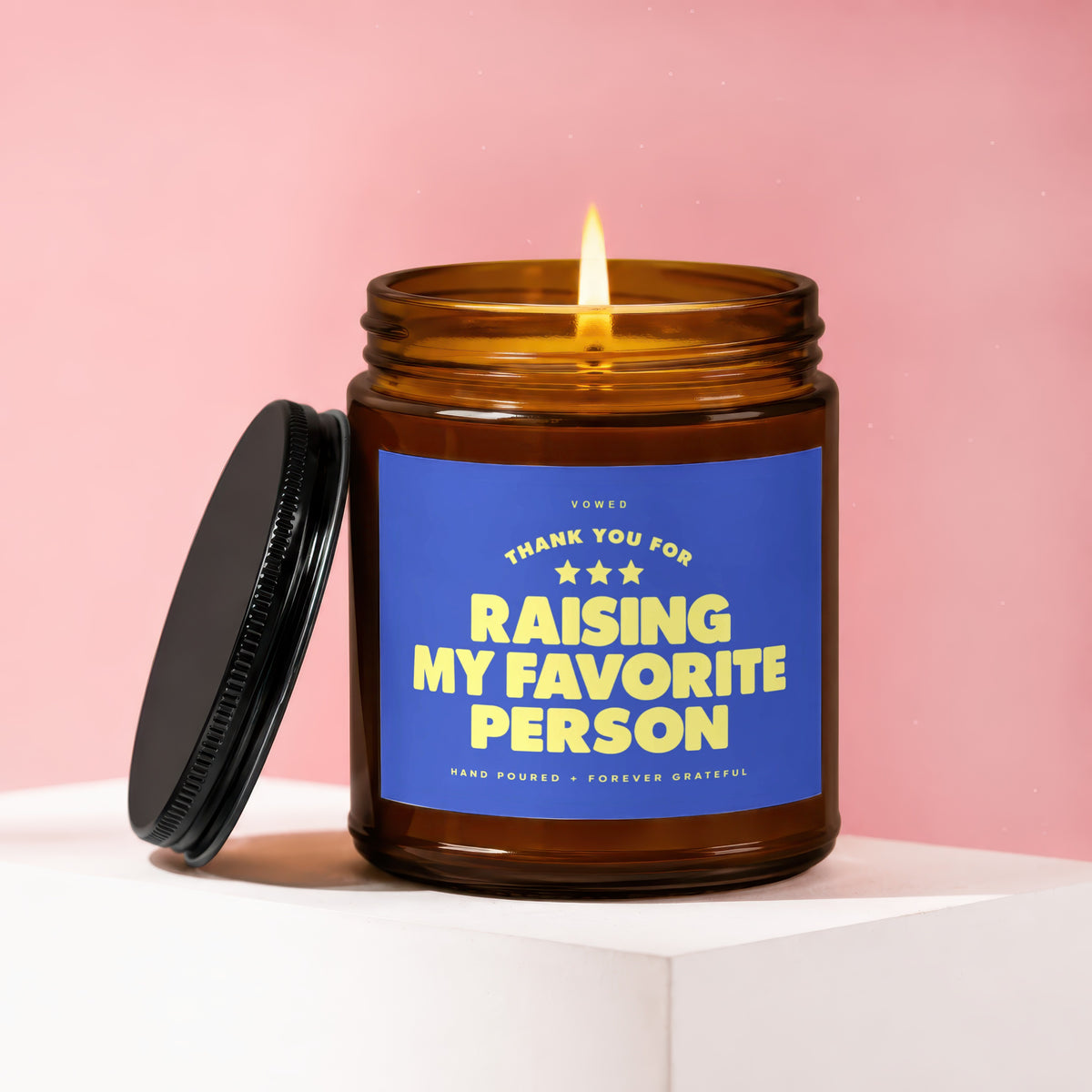 Amber candle with lit wick and blue label reading "Thank you for raising my favorite person".