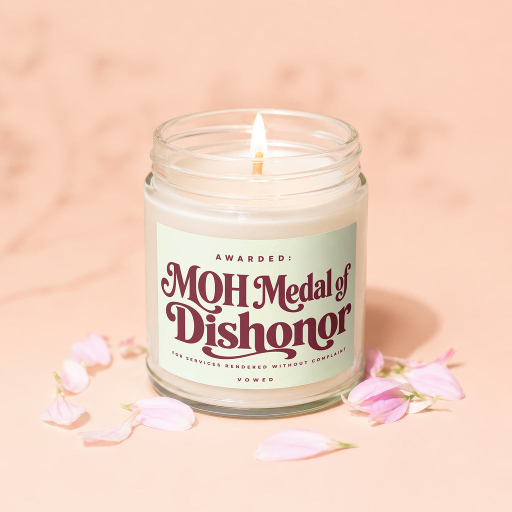 Lit candle in glass jar with "MOH Medal of Dishonor" label and petals.