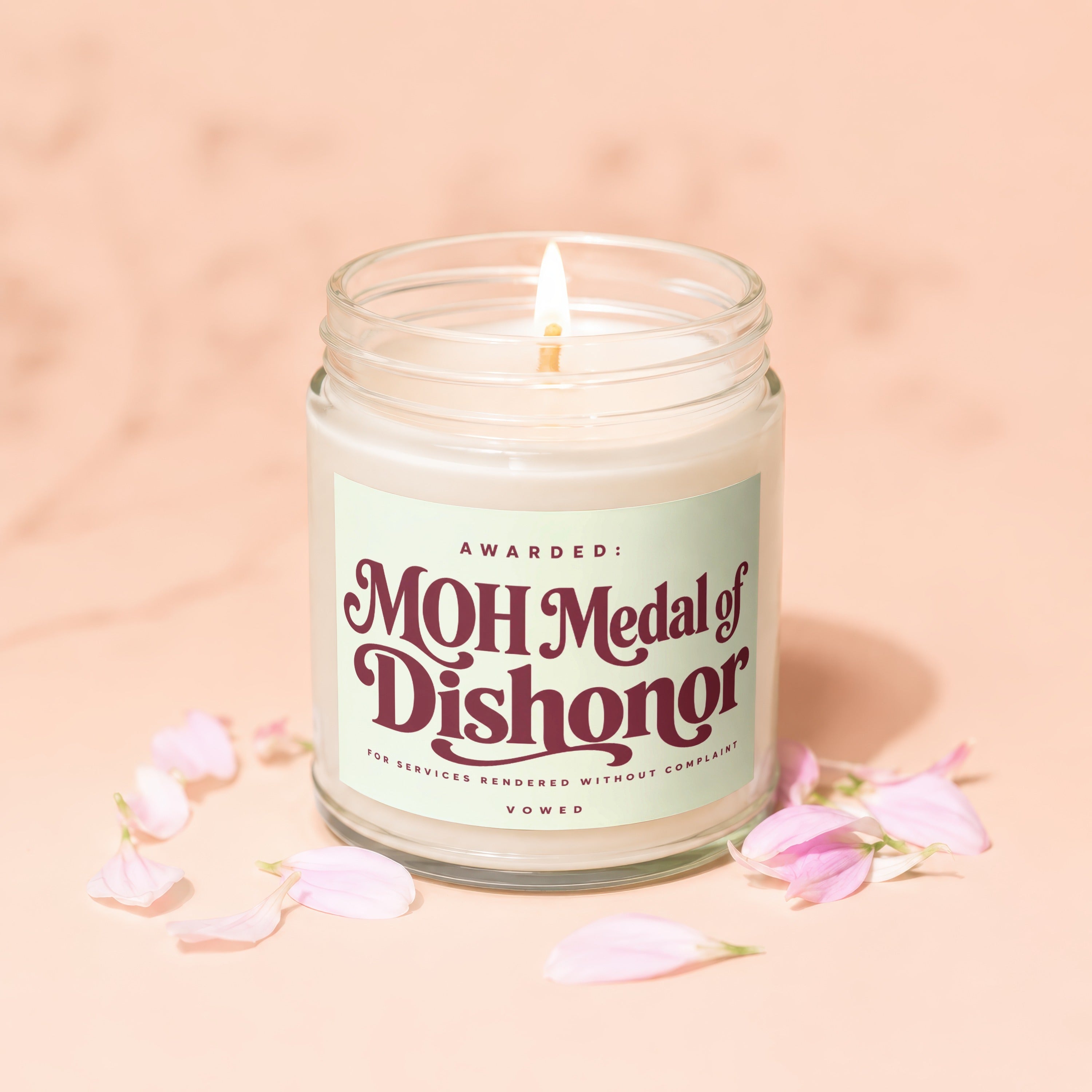 Lit candle in glass jar with "MOH Medal of Dishonor" label and petals.