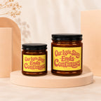Two amber glass candles with yellow labels reading "Our Love Story - Ends Continues".