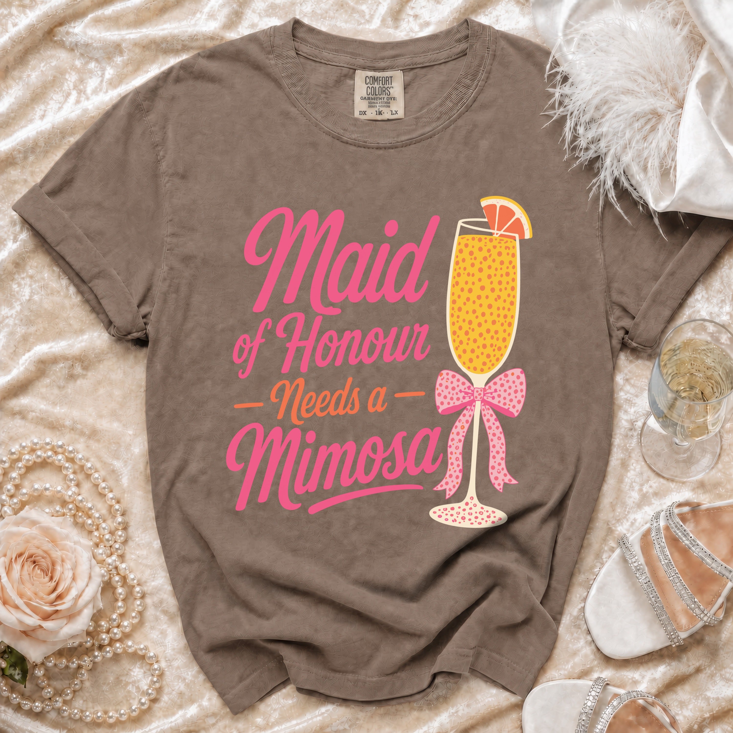 Brown t-shirt with pink text "Maid of Honour Needs a Mimosa" and a mimosa graphic.