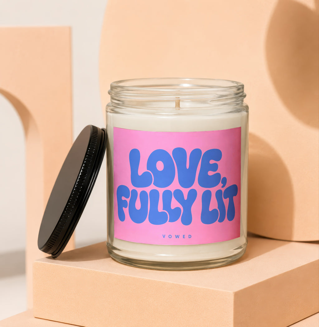 Glass candle with pink label that says "LOVE, FULLY LIT" and "VOWED".