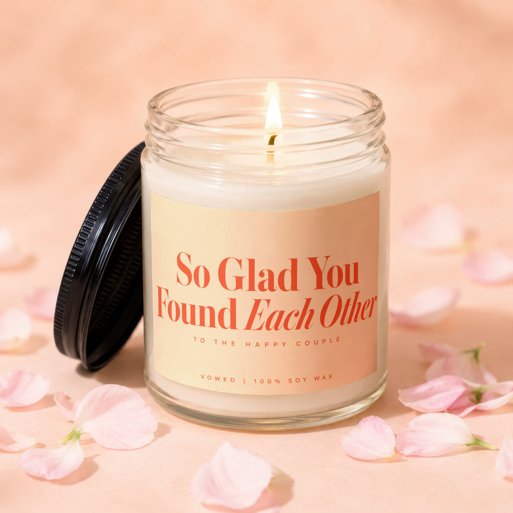 Soy wax candle with "So Glad You Found Each Other" text, among pink petals.