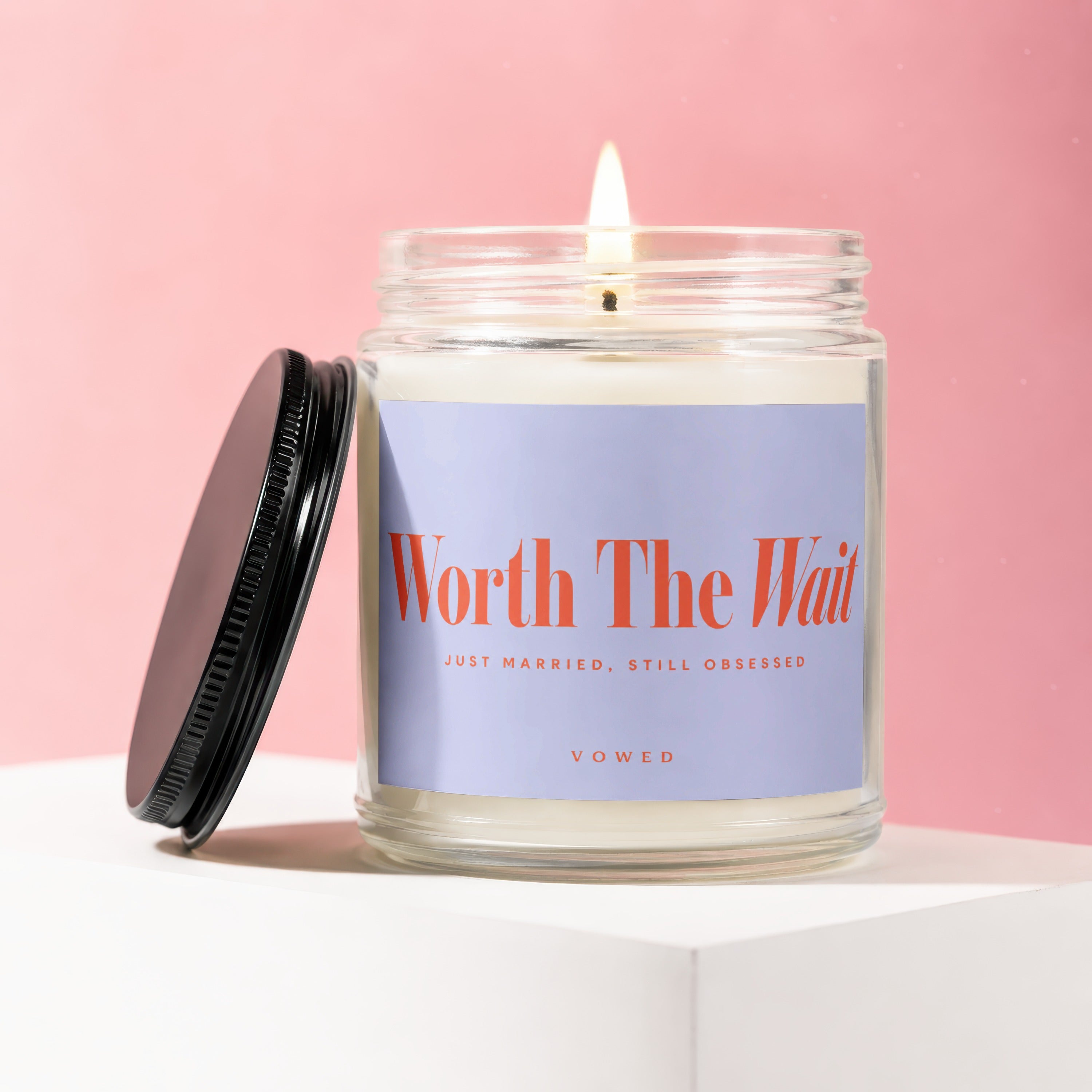 Candle with a lit wick and lid off, labeled "Worth The Wait"