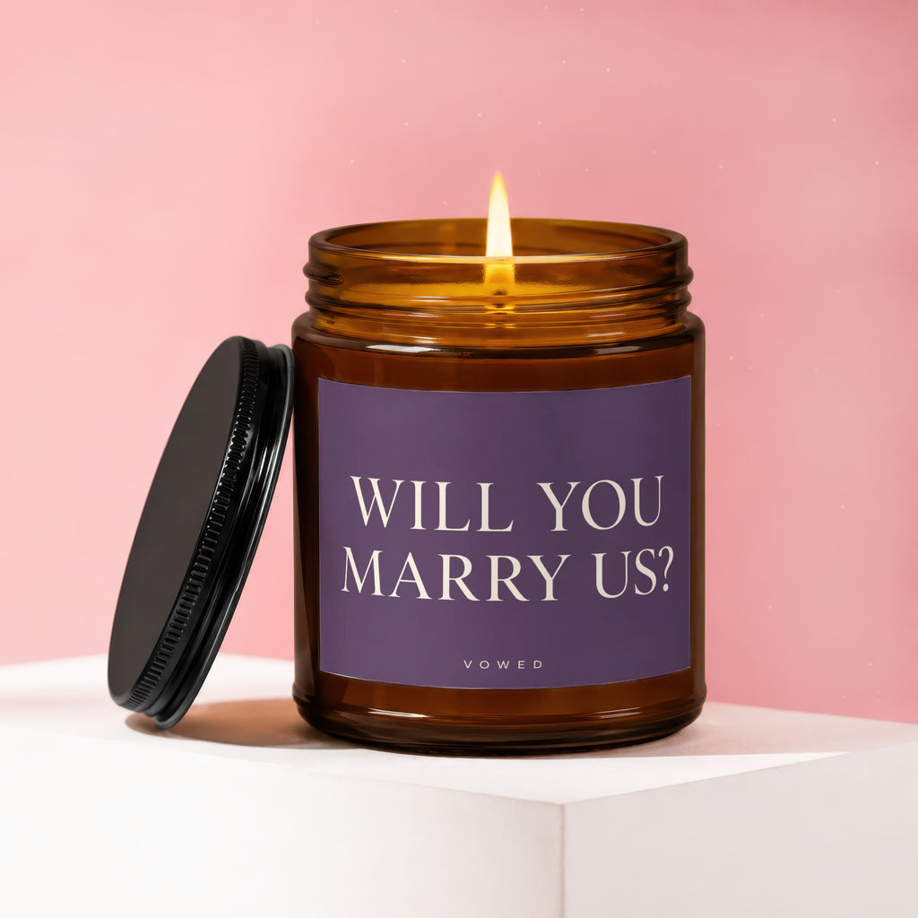 Candle with lit wick and lid off, text "WILL YOU MARRY US?"