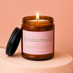 Amber jar candle with lit wick and "bridesmaid noun" definition label.