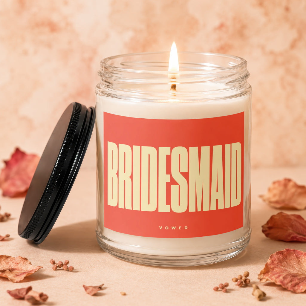 Glass jar candle with "BRIDESMAID" text, lit wick, and black lid.