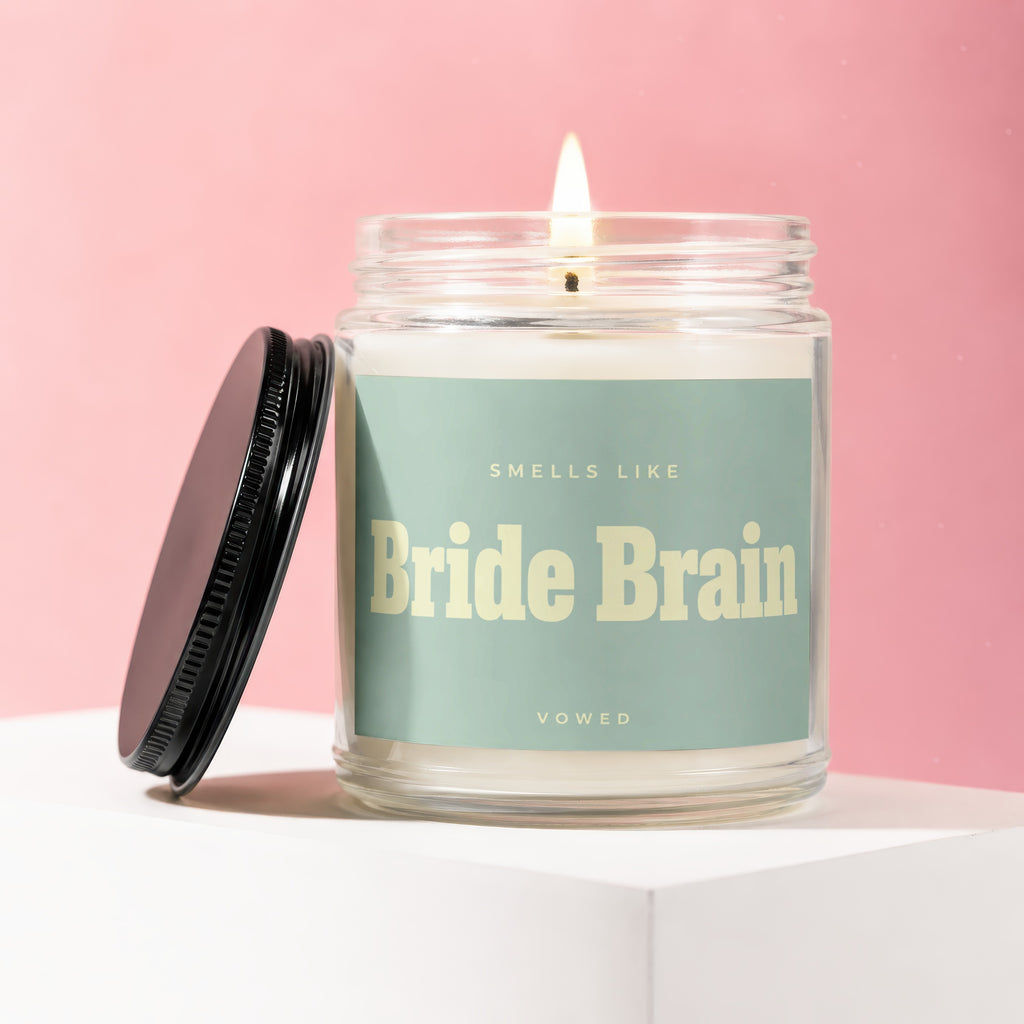 Candle with lit wick and black lid, says "Smells Like Bride Brain Vowed"