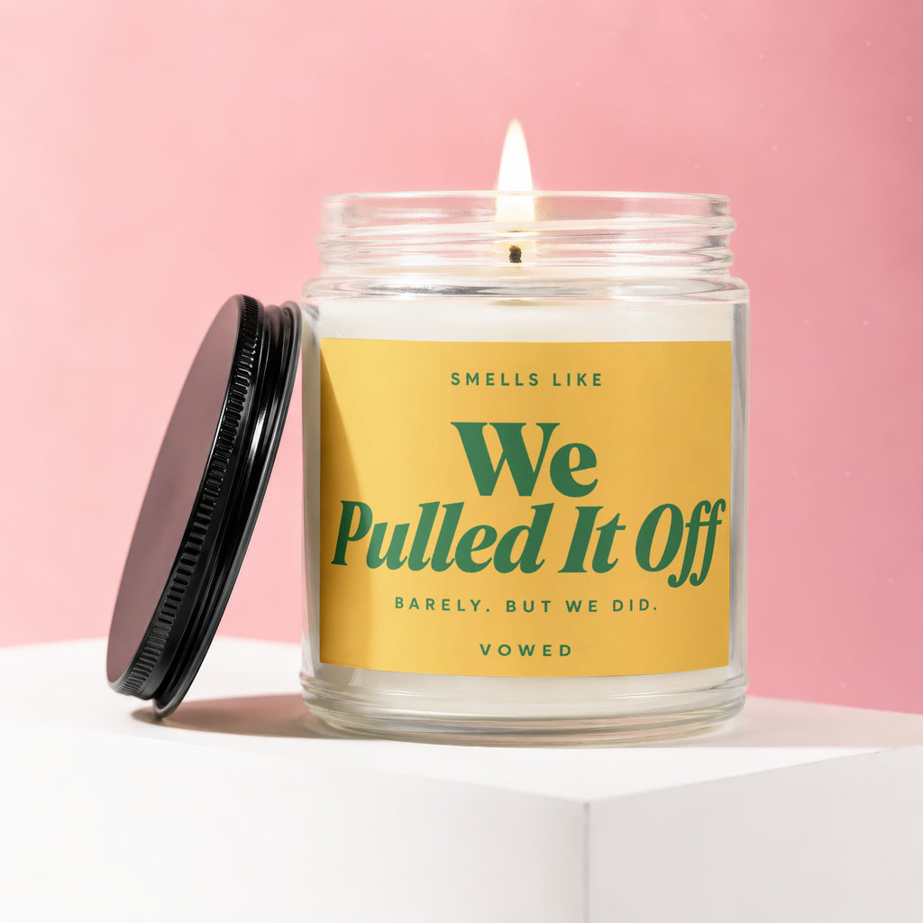 Glass jar candle with lid off, reads "Smells Like We Pulled It Off".