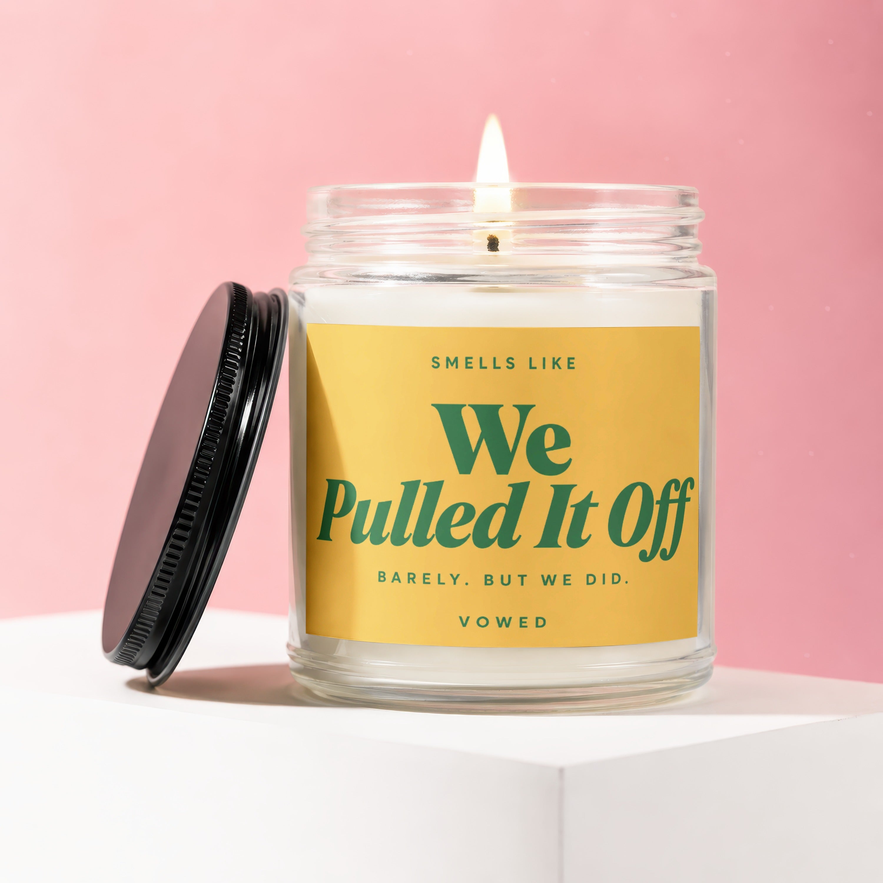 Glass jar candle with lid off, reads "Smells Like We Pulled It Off".