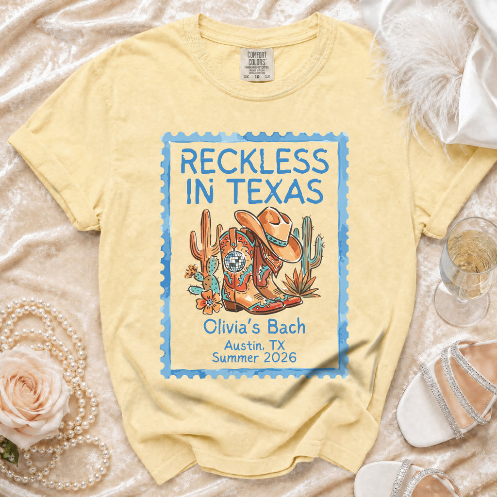 T-shirt with Texas-themed graphic: cowboy boots, hat, cactus, and text "Reckless in Texas".
