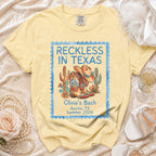 T-shirt with Texas-themed graphic: cowboy boots, hat, cactus, and text "Reckless in Texas".