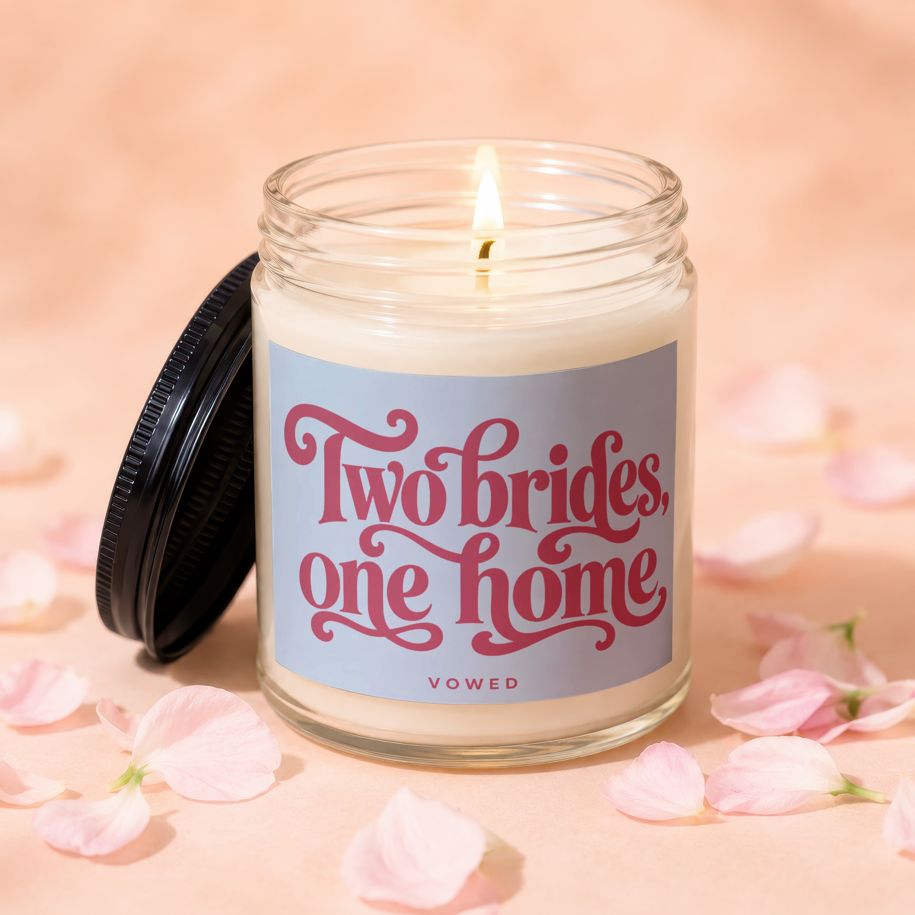 Glass candle with lid off, displaying text "Two brides, one home"