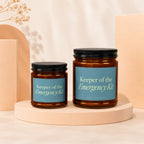 Two amber glass candles with blue labels reading "Keeper of the Emergency Kit".