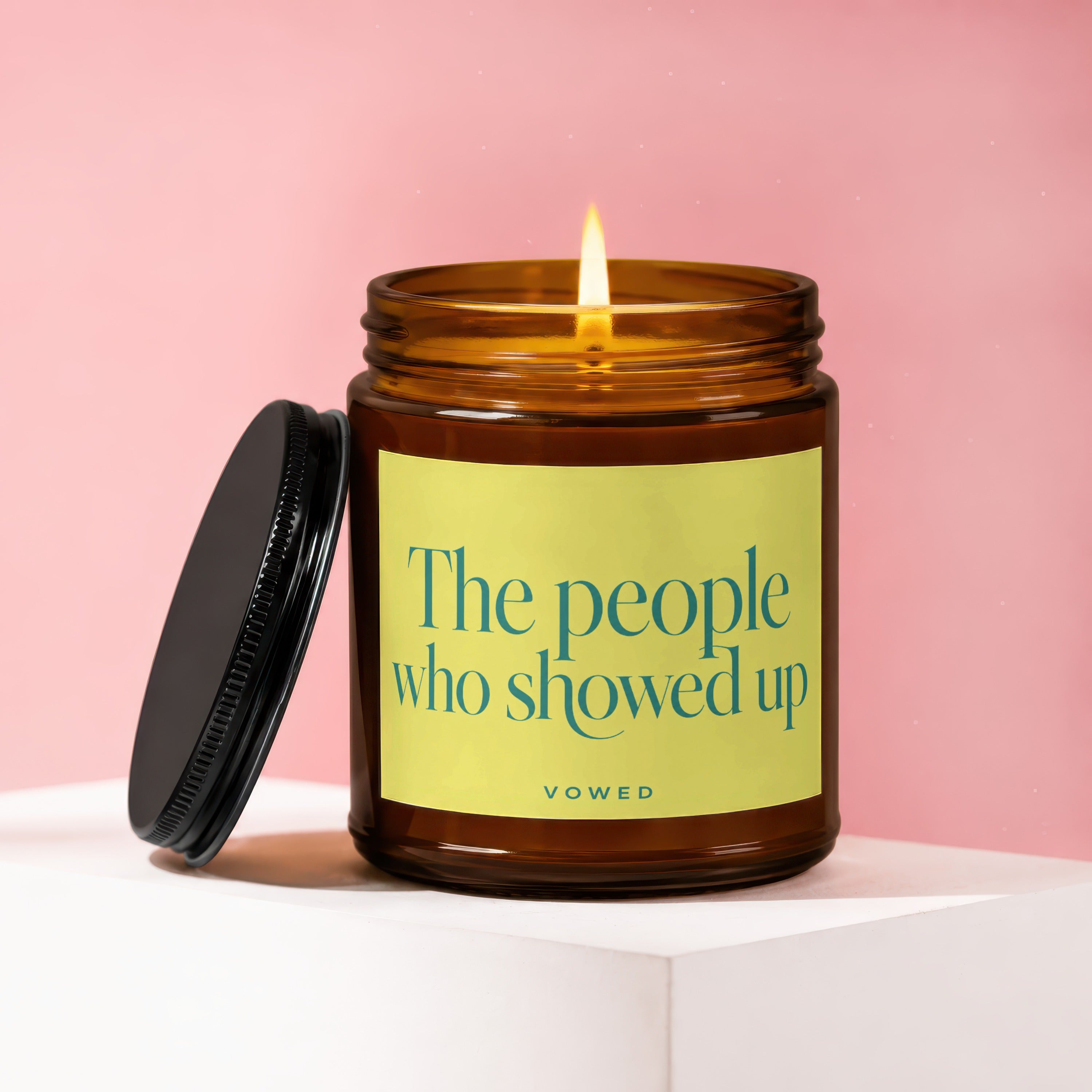 An amber candle with a lit wick and black lid, labeled "The people who showed up"