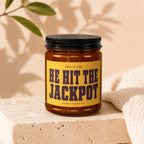 Amber jar candle with "Smells like HE HIT THE JACKPOT" on yellow label.