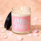 Candle with "Mrs & Mrs Vowed" text on pink label, lid off, surrounded by petals.