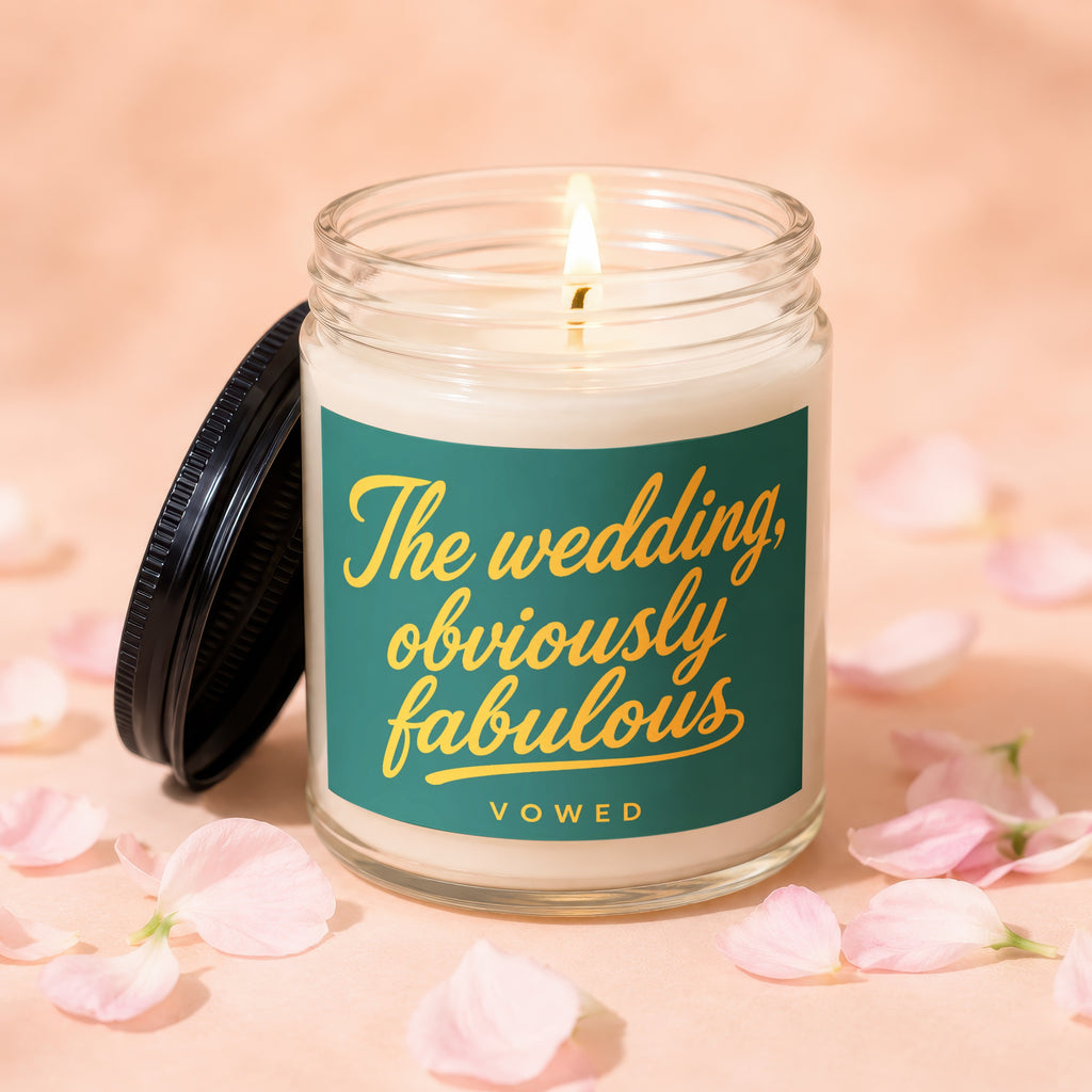 Candle with "The wedding, obviously fabulous" text and lit wick, surrounded by pink petals.