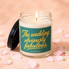 Candle with "The wedding, obviously fabulous" text and lit wick, surrounded by pink petals.