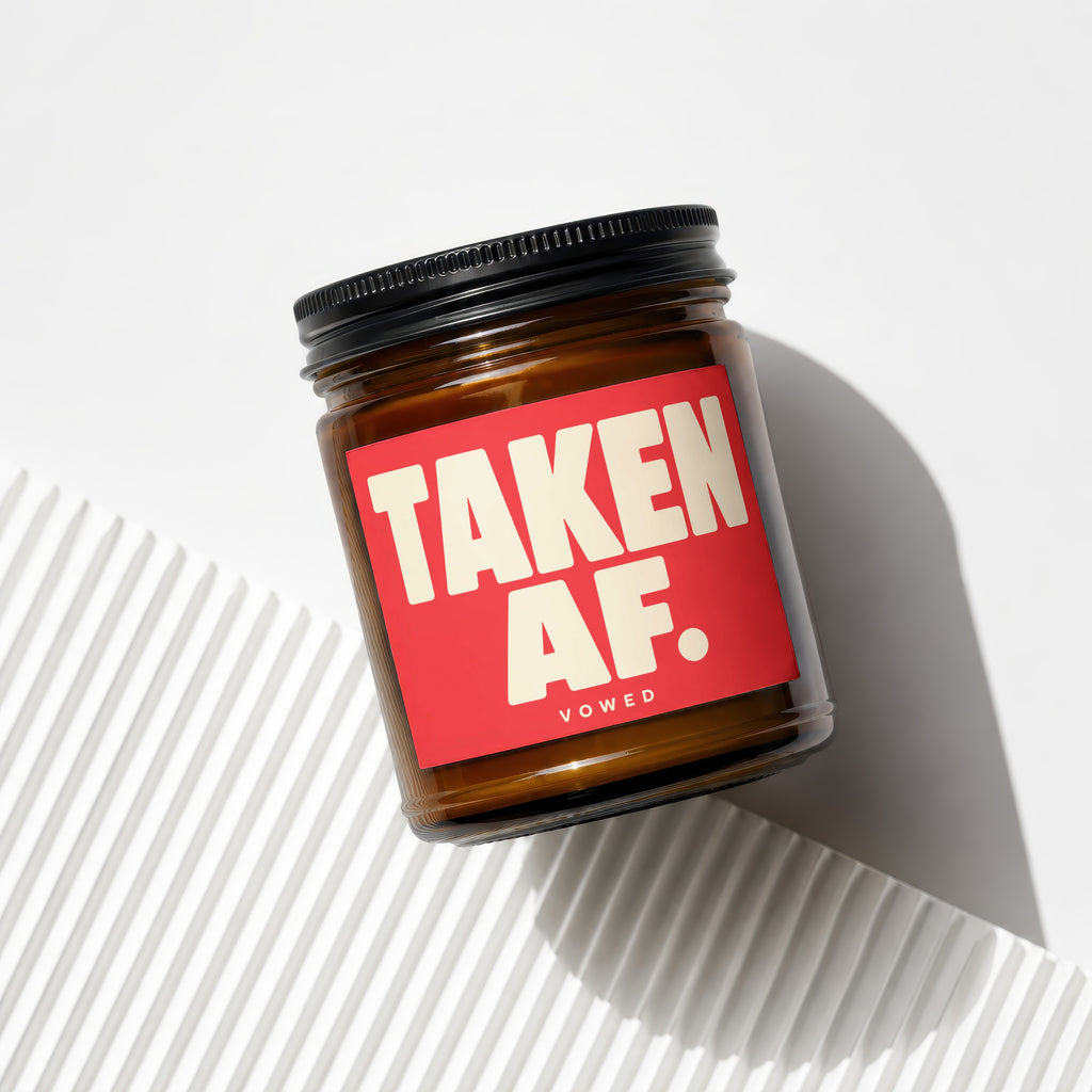 Amber jar candle with red label reading "TAKEN AF. VOWED."