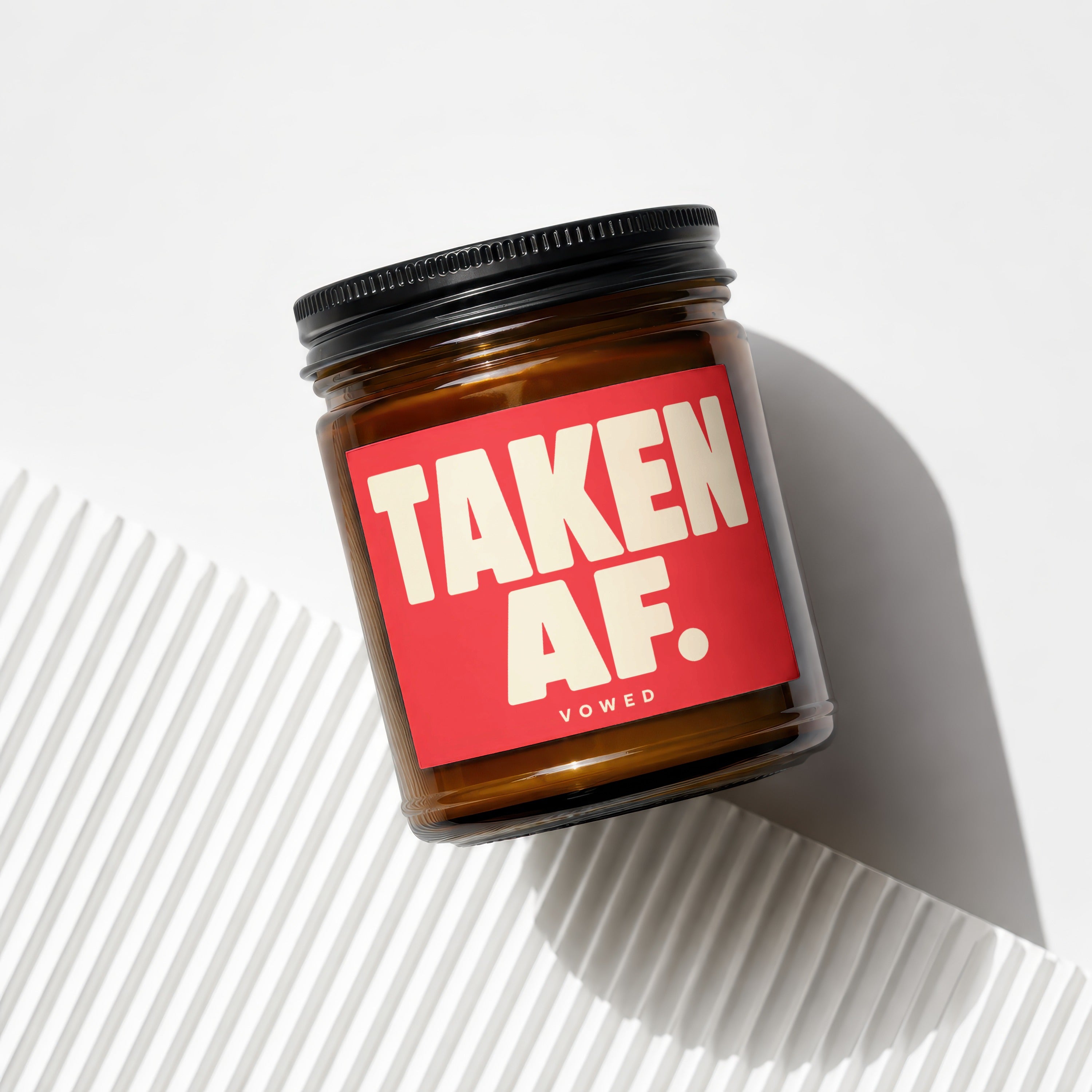 Amber jar candle with red label reading "TAKEN AF. VOWED."