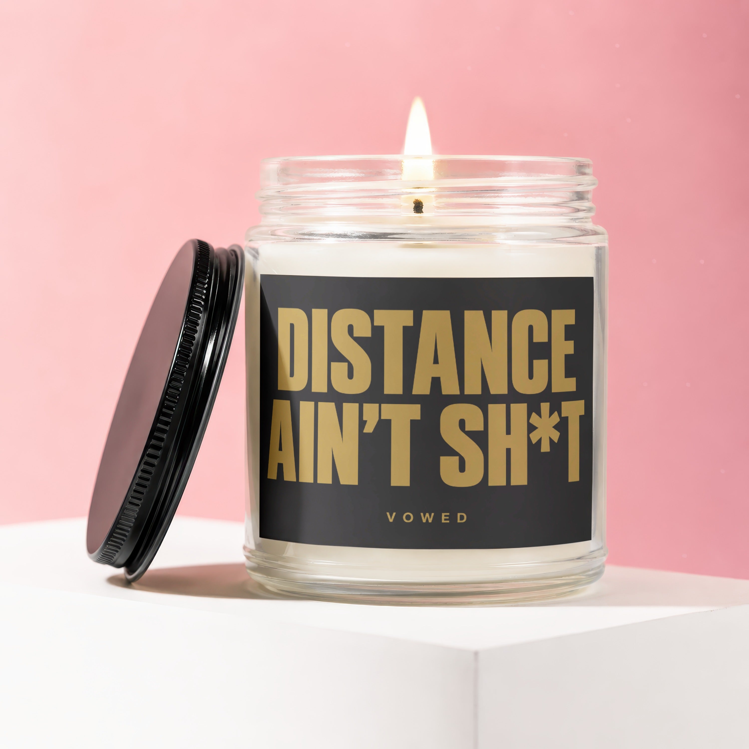 Glass candle with lit wick, black lid, and "DISTANCE AIN'T SH*T" text.