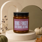 Amber candle in glass jar with pink label reading "RING FINGER OVERHEATING".