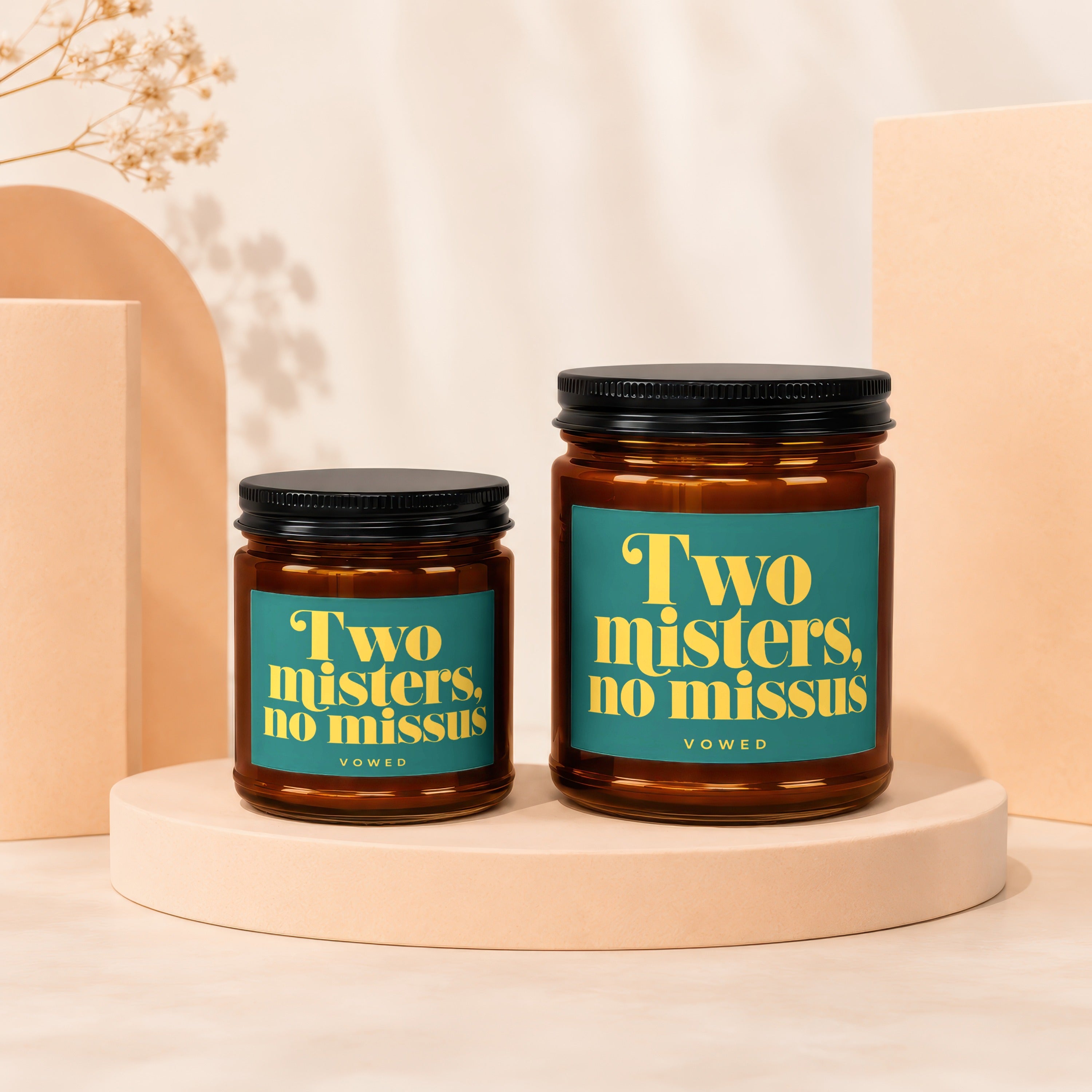 Two amber glass candles with black lids and teal labels that read "Two misters, no missus."