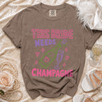Brown t-shirt with pink and purple text: "THIS BRIDE NEEDS CHAMPAGNE".