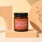 VOWED candle with "Partners, officially" text on a coral label.