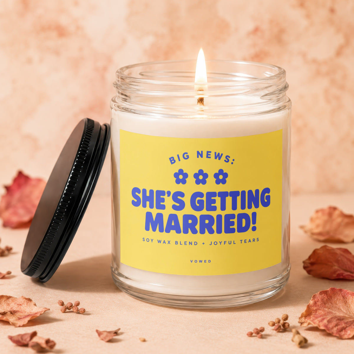 Glass candle with a lit wick and yellow label reading "She's Getting Married!"