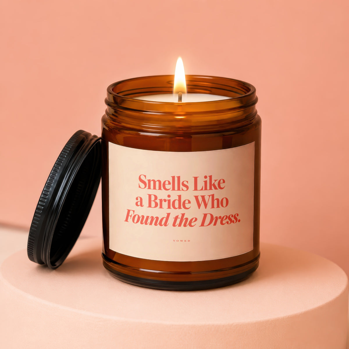 Amber jar candle with lit wick and text "Smells Like a Bride Who Found the Dress."