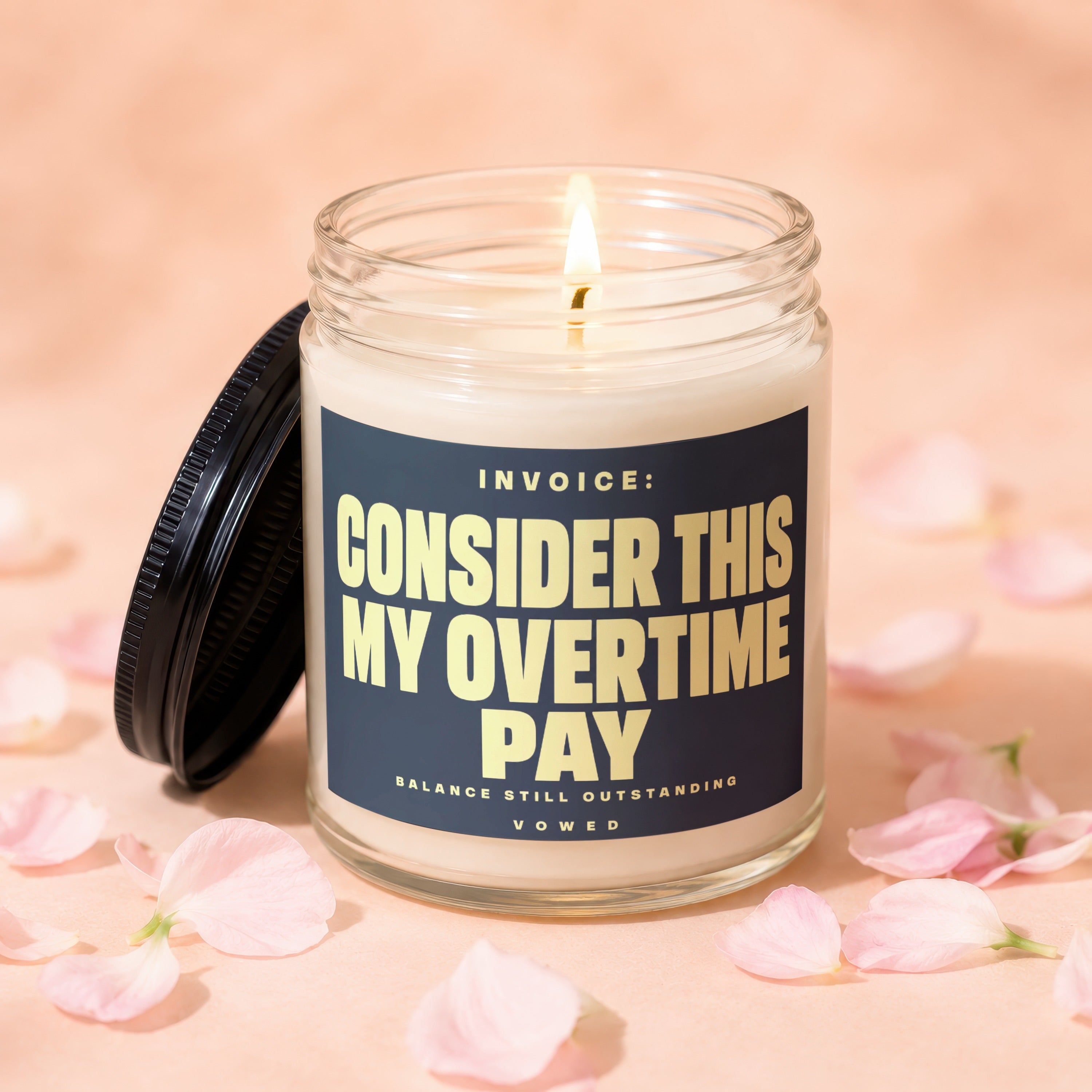 Glass candle with lit wick, black lid, and dark blue label with gold text.