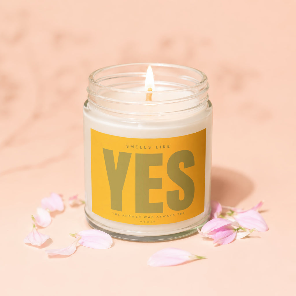 A lit candle in a glass jar with "Smells Like YES" on the label.