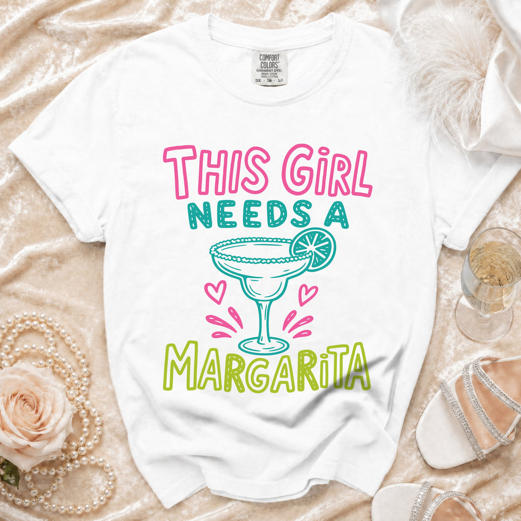 White t-shirt with "This Girl Needs a Margarita" graphic and margarita illustration.