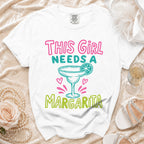 White t-shirt with "This Girl Needs a Margarita" graphic and margarita illustration.