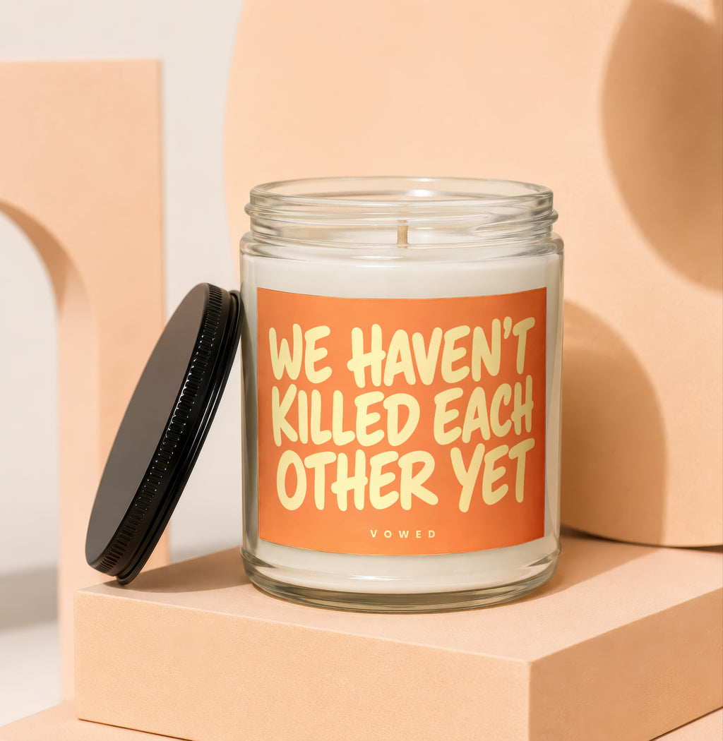 Candle with "WE HAVEN'T KILLED EACH OTHER YET" text and black lid.
