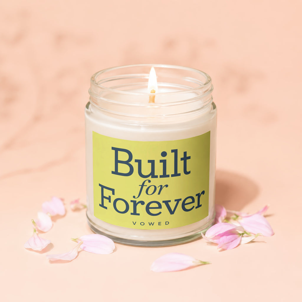 Glass jar candle with lit wick, green label reads "Built for Forever VOWED."