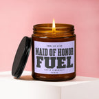 Amber candle with lit wick, lid off, labeled "Maid of Honor Fuel".