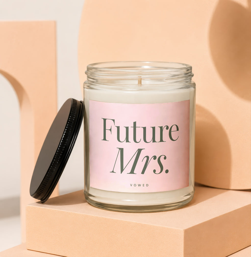 "Future Mrs." candle in a glass jar with black lid, displayed on peach blocks.