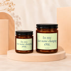 Two amber glass candles with black lids and pale green labels reading "In my last-name-changing era."