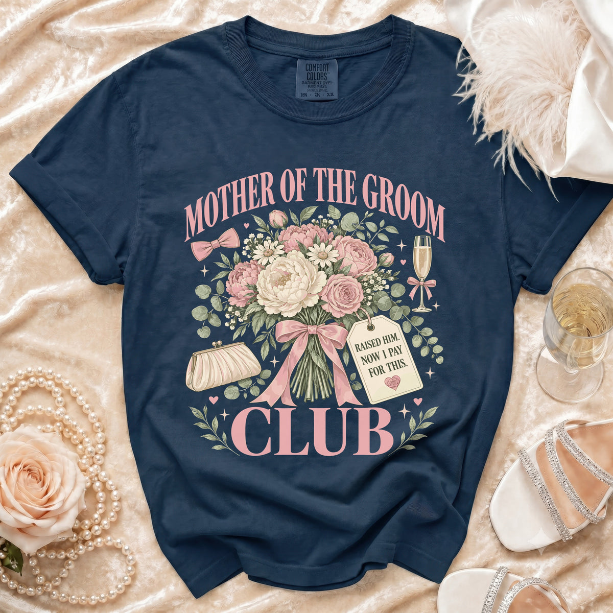 A dark blue t-shirt printed with a pink floral bouquet, champagne glass, clutch, and text reading Mother of the Groom Club.