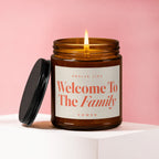 Amber jar candle with lit flame and lid. Label reads "Welcome To The Family VOWED".