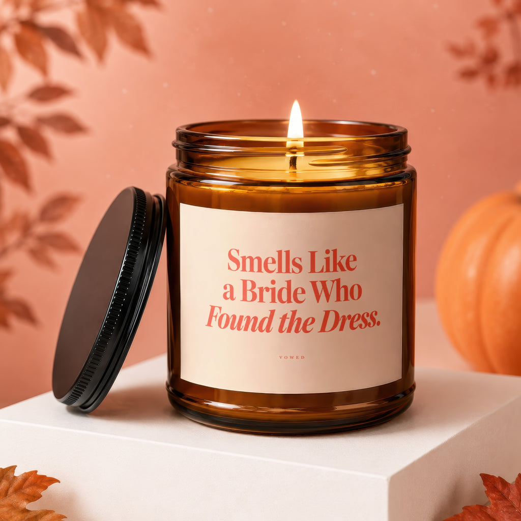 Amber candle with lit wick, reads "Smells Like a Bride Who Found the Dress."