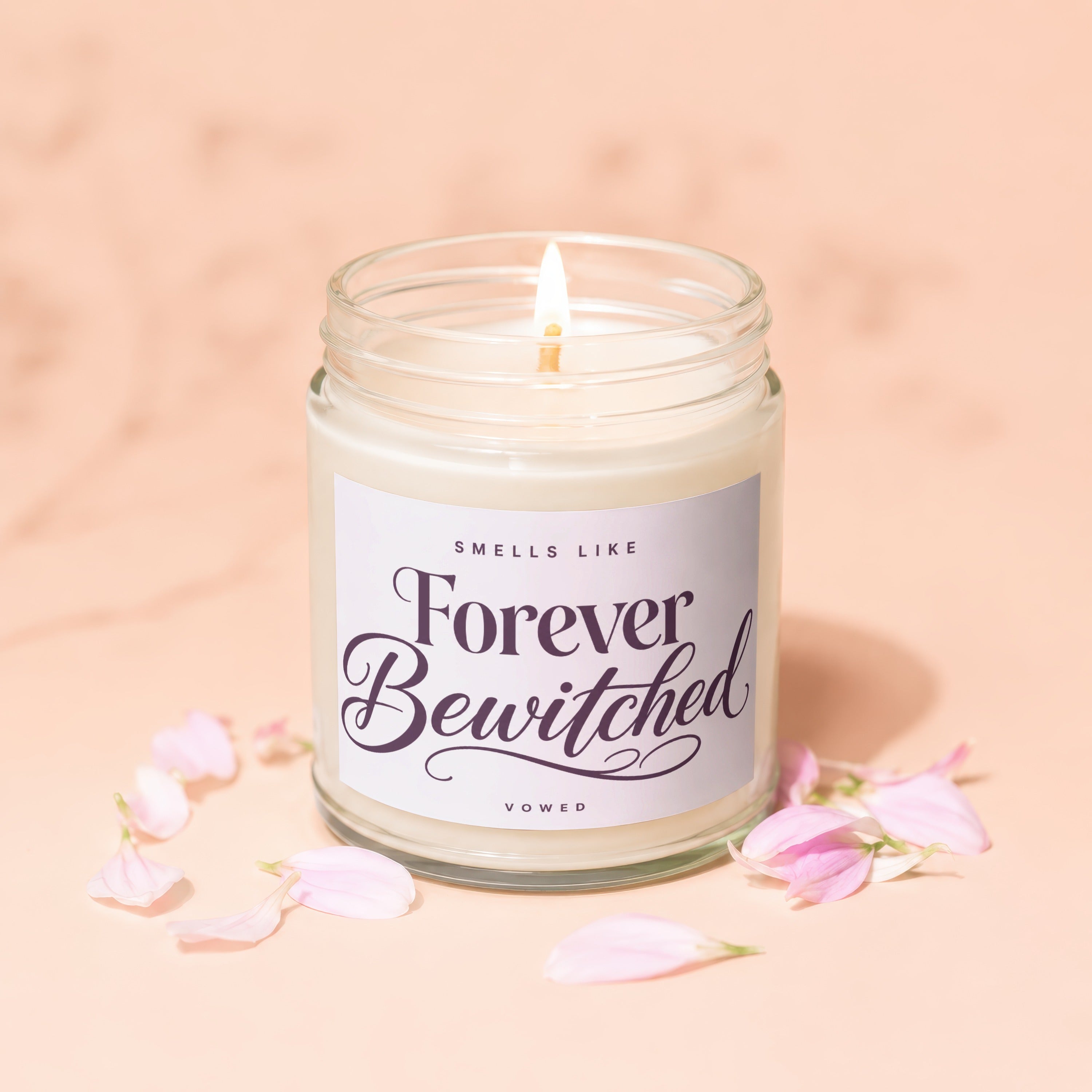 Lit candle in glass jar with "Forever Bewitched" label, surrounded by pink petals.