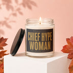 Lit candle with label "Chief Hype Woman" on a white pedestal, surrounded by fall leaves.