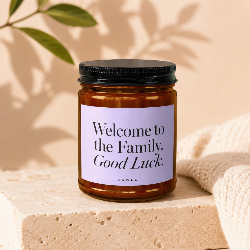 Amber candle in glass jar with lavender label stating "Welcome to the Family. Good Luck."
